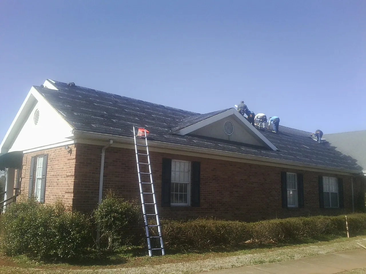 Crew tearing shingles off a brick ranch roof with a ladder set — Metal Roof Repair work by our crew in Kerman