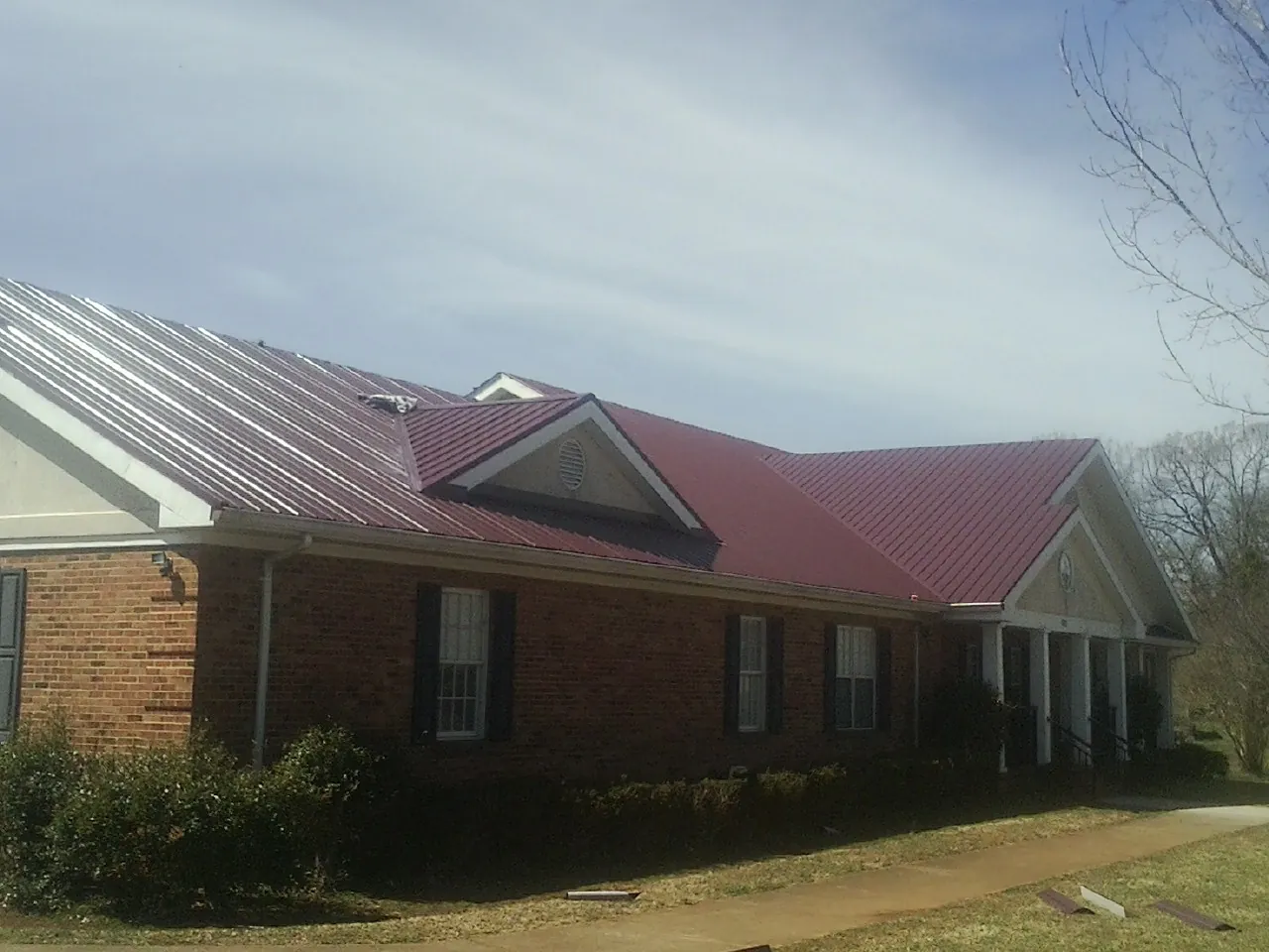 Red metal roof with gabled entries on a long brick building, from a Hail Damage Roof Repair job in Kerman