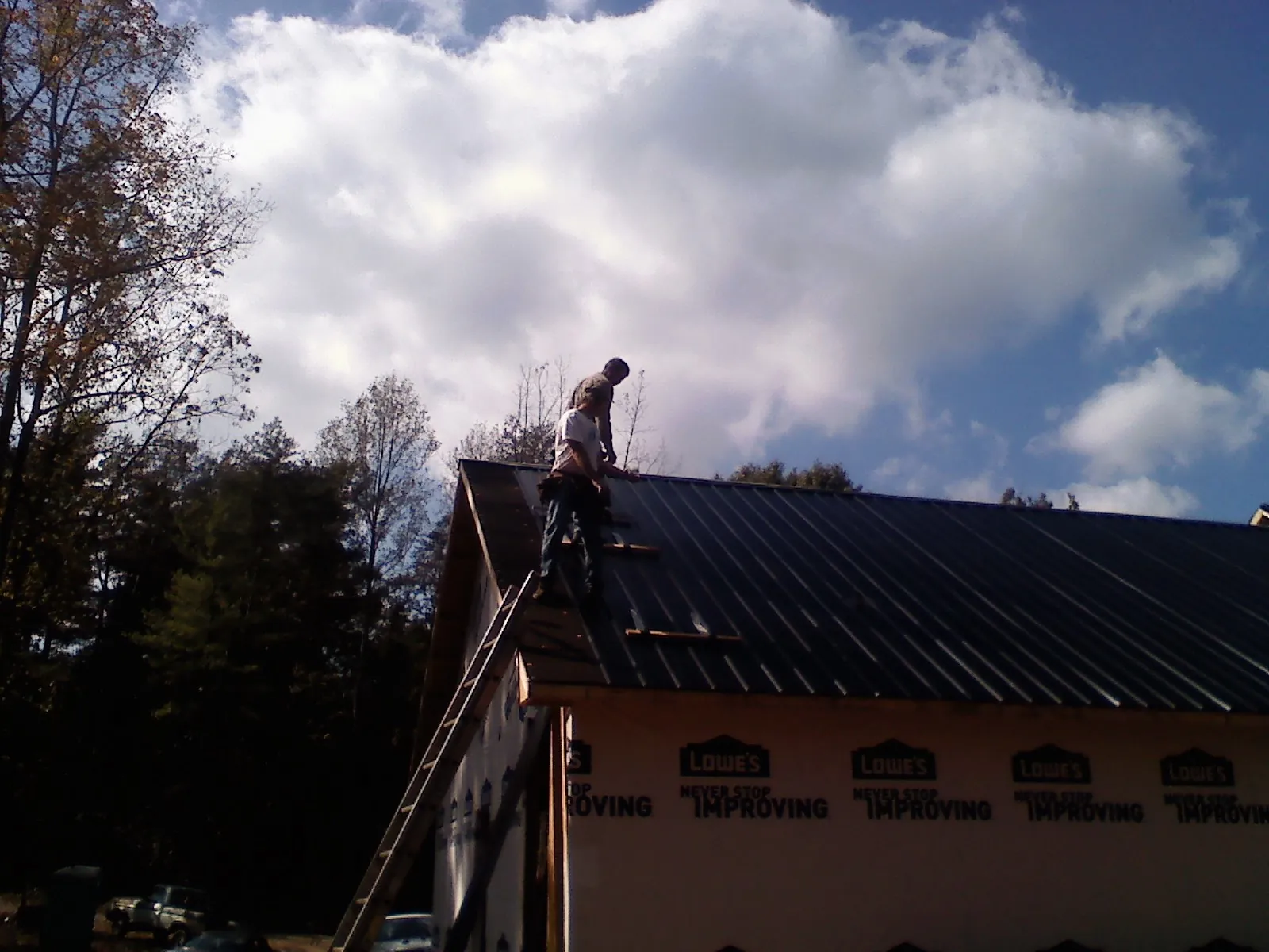 Roofer fastening dark metal panels high against a cloudy sky, from a Roof Inspection job in Kerman