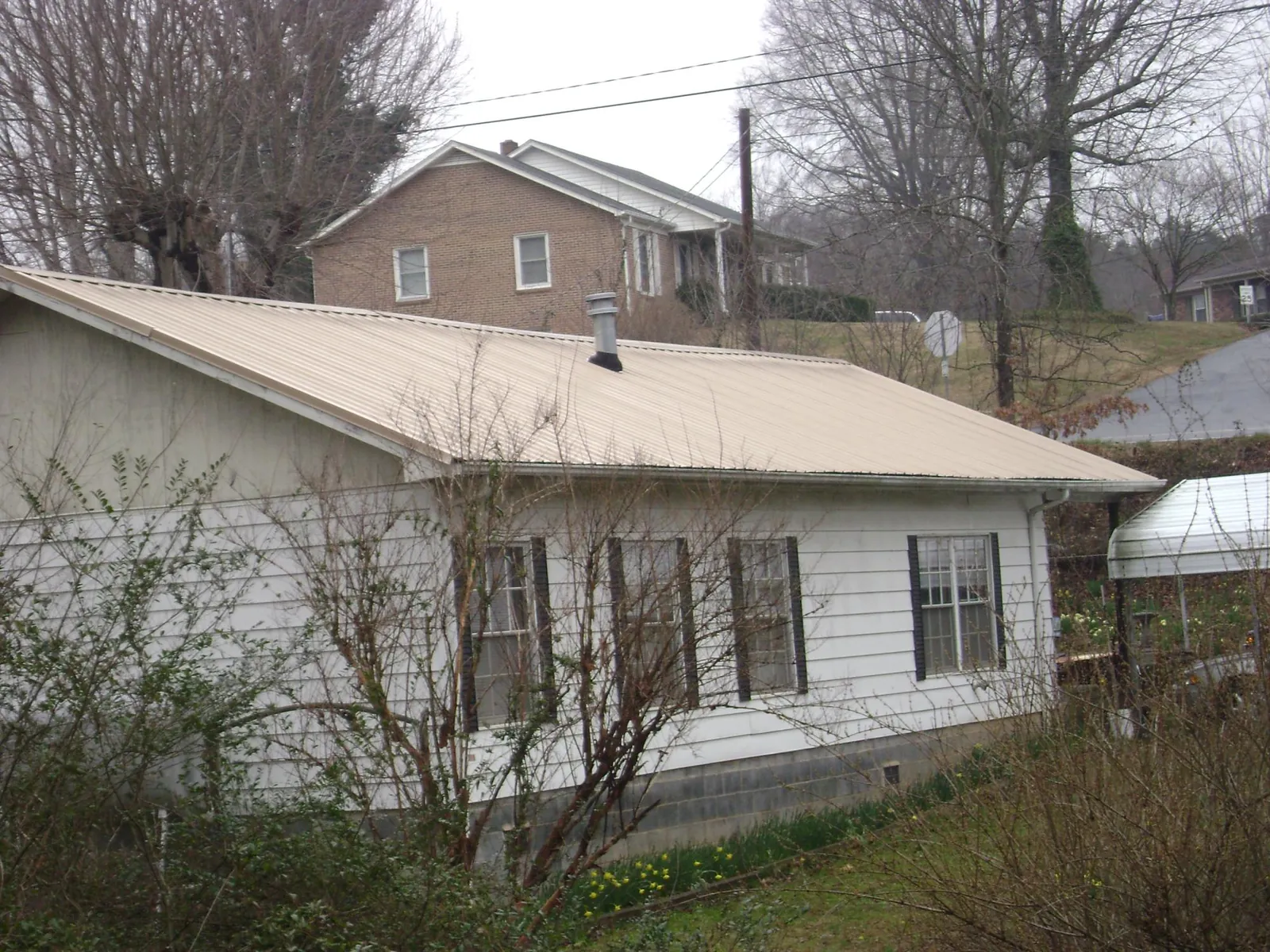 Tan metal roof on a white sided house set into a hillside — Commercial Roofing by Roofing Brothers in Kerman